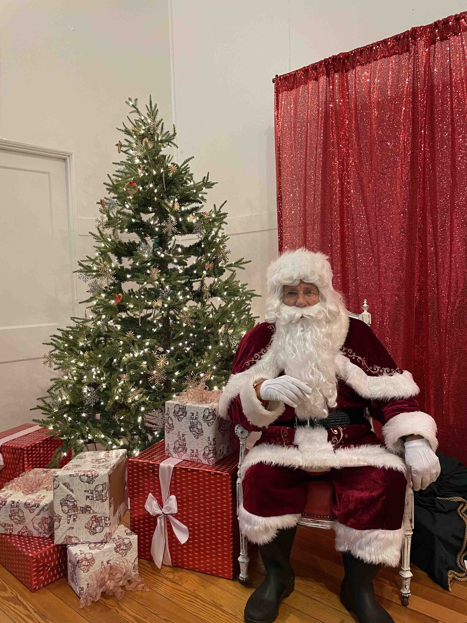 Santa sitting by a Christmas Tree with presents under it